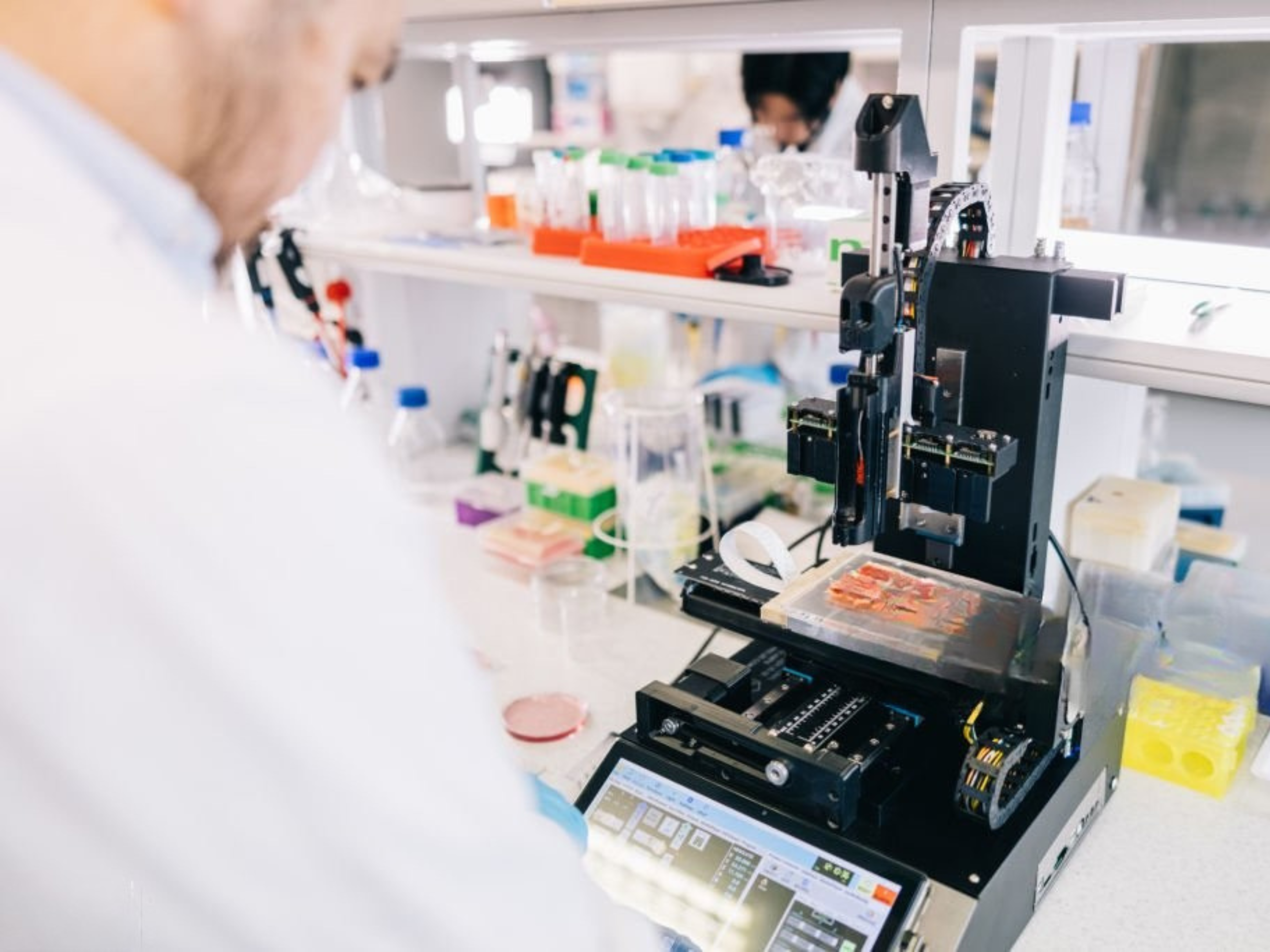 A man wearing a lab coat is engaged in operating a testing and measurement device in a scientific setting